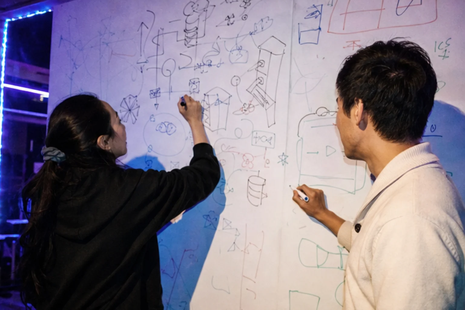 Two builders sketching on a crowded whiteboard